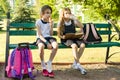Attractive little girlfriends schoolgirls with backpacks, Girls rest on bench in the park after school, eat ice cream, drink water Royalty Free Stock Photo
