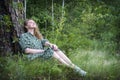 Attractive girl in the forest in a dress sits under a tree in the grass Royalty Free Stock Photo