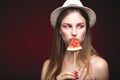 Attractive Lovely girl with pink make up, wearing jeans, hat and top, posing at red studio background, holding slice watermelon Royalty Free Stock Photo