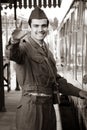 Handsome male British soldier in WW2 vintage uniform at train station next to train, waving and smiling