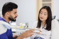 Attractive male dentist checking and selecting color of young asian woman teeth.