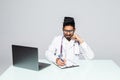 Attractive indian male physician writes a prescription on desk over blue background Royalty Free Stock Photo