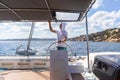 Attractive male skipper navigating the fancy catamaran sailboat on sunny summer day on calm blue sea water.