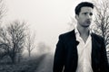 Handsome man wearing suit walking on a lonely foggy road Royalty Free Stock Photo