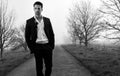 Handsome man wearing suit walking on a lonely foggy road Royalty Free Stock Photo