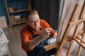 Attractive man artist painting on canvas on the easel at home studio using painter palette. having classes at art studio Royalty Free Stock Photo