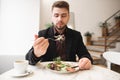 Attractive man with a beard eating a diet salad in a cozy restaurant. Man took the green salad on the fork Royalty Free Stock Photo