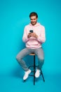 Attractive man chatting or typing text message using cell phone isolated over light blue background. Royalty Free Stock Photo