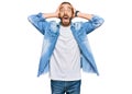 Attractive man with long hair and beard wearing casual denim jacket crazy and scared with hands on head, afraid and surprised of