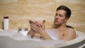 Attractive man rubbing hypoallergenic cosmetic into skin taking bath, smoothing