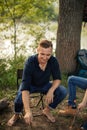 Attractive man in shirt and jeans sitting around a campfire