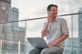 Man on the street. Attractive man sitting outside, using mobile phone and laptop, smiling and looking away Royalty Free Stock Photo