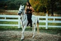 Attractive man sitting on white horse on the ranch in autumn. Full length of young handsome man sitting on his stallion Royalty Free Stock Photo