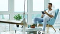 Attractive man using digital tablet sitting in chair at balcony in loft modern apartment Royalty Free Stock Photo