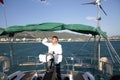 Attractive man in white stands at the helm of a yacht at sea and looks at the horizon with his hand raised Sailing, tourism travel