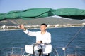 Attractive man in white stands at the helm of a yacht at sea and looks at the horizon with his hand raised Sailing, tourism travel