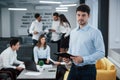 Attractive manager ready to answer your questions. Portrait of young guy stands in the office with employees at