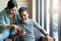 Attractive mature asian man with white stylish short beard looking at smartphone computer with teenage eye glasses hipster woman Royalty Free Stock Photo