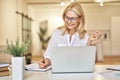 Attractive mature businesswoman smiling and making notes while having online video call using laptop, sitting at her Royalty Free Stock Photo