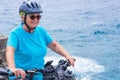 Attractive mature cyclist woman enjoying activity at sea with her electro bike. Standing on the cliff