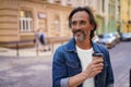 Attractive mature freelancer man smiling looking sideways holding disposable paper cup with hot coffee standing at old Royalty Free Stock Photo