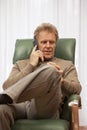 Attractive mature man talking on smartphone in a chair in a living room