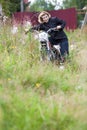 Attractive mature woman posing with motocross motorcycle in high grass, holding the wheel and looking at camera