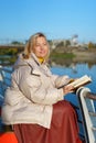 Attractive mature woman reading a book on the river bank. Moment of leisure. Outdoor relax. Royalty Free Stock Photo