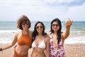 Attractive mature woman next to two young, pretty, brunette South American women in bikinis and sunglasses taking funny pictures Royalty Free Stock Photo