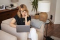 Attractive mid aged woman with notebook and smartphone sitting in an armchair and working from home Royalty Free Stock Photo