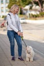 Attractive middle-aged blond woman walking with fluffy white dog in summer city