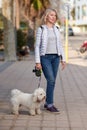 Attractive middle-aged blond woman walking with fluffy white dog in summer city