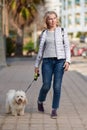 Attractive middle-aged blond woman walking with fluffy white dog in summer city