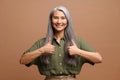Attractive middle-aged 50s woman with long grey hair showing thumbs up and looking at camera with toothy smile, lady Royalty Free Stock Photo