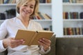 Attractive middle aged woman enjoying reading a book sitting on the sofa in her living room smiling while she reading Royalty Free Stock Photo