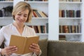 Attractive middle aged woman enjoying reading a book sitting on the sofa in her living room smiling while she reading Royalty Free Stock Photo