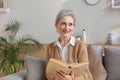 Attractive middle aged woman enjoying reading a book sitting on the sofa in her living room smiling while she reading Royalty Free Stock Photo