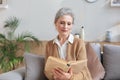 Attractive middle aged woman enjoying reading a book sitting on the sofa in her living room smiling while she reading Royalty Free Stock Photo