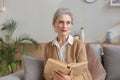 Attractive middle aged woman enjoying reading a book sitting on the sofa in her living room smiling while she reading. Royalty Free Stock Photo