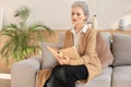 Attractive middle aged woman enjoying reading a book sitting on the sofa in her living room smiling while she reading. Royalty Free Stock Photo