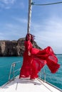 Attractive middle-aged woman in a red dress on a yacht on a summer day. Luxury summer adventure, outdoor activities. Royalty Free Stock Photo