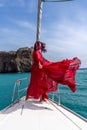 Attractive middle-aged woman in a red dress on a yacht on a summer day. Luxury summer adventure, outdoor activities. Royalty Free Stock Photo