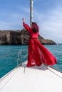 Attractive middle-aged woman in a red dress on a yacht on a summer day. Luxury summer adventure, outdoor activities. Royalty Free Stock Photo