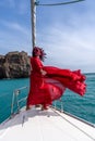 Attractive middle-aged woman in a red dress on a yacht on a summer day. Luxury summer adventure, outdoor activities. Royalty Free Stock Photo