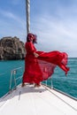 Attractive middle-aged woman in a red dress on a yacht on a summer day. Luxury summer adventure, outdoor activities. Royalty Free Stock Photo