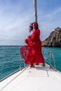 Attractive middle-aged woman in a red dress on a yacht on a summer day. Luxury summer adventure, outdoor activities. Royalty Free Stock Photo