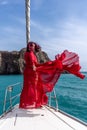 Attractive middle-aged woman in a red dress on a yacht on a summer day. Luxury summer adventure, outdoor activities. Royalty Free Stock Photo