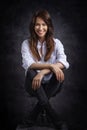 Studio portrait of a brunette haired attractive woman wearing white shirt and black jeans while posing at isolated dark background Royalty Free Stock Photo