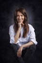 Studio portrait of a brunette haired attractive woman wearing white shirt and black jeans while posing at isolated dark background Royalty Free Stock Photo