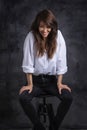 Studio portrait of a brunette haired attractive woman wearing white shirt and black jeans while posing at isolated dark background Royalty Free Stock Photo